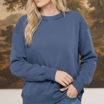 A woman wearing a graced indigo crewneck pullover top with ribbed cuffs and a classic neckline, styled with jeans.