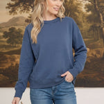 A woman wearing a graced indigo crewneck pullover with a ribbed neckline and cuffs, styled with blue denim jeans.