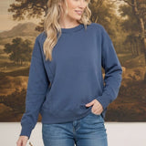 A woman wearing a graced indigo crewneck pullover with a ribbed neckline and cuffs, styled with blue denim jeans.