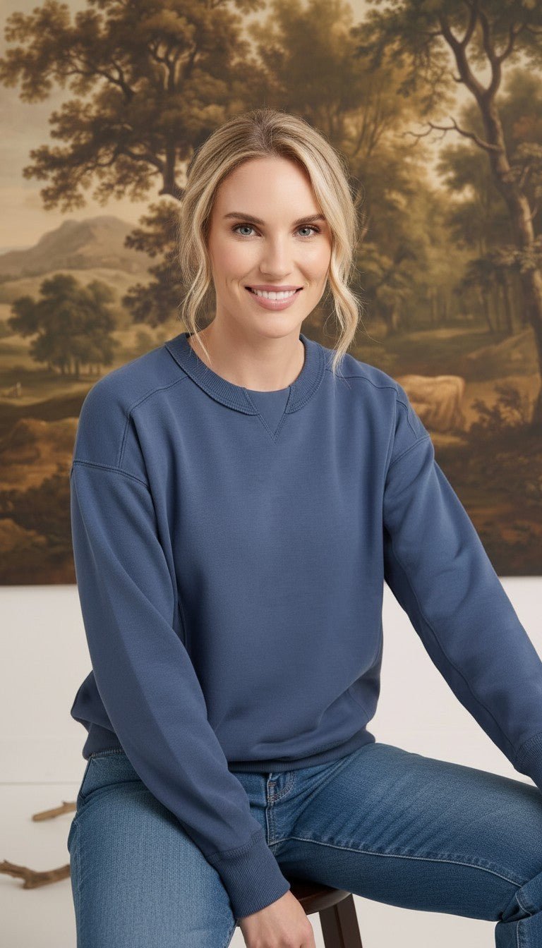 A woman wearing a graced indigo crewneck pullover with ribbed trim, styled with jeans in a studio setting.