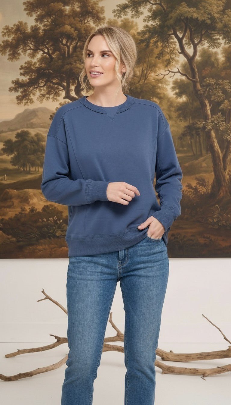 A woman wearing a graced indigo crewneck pullover with ribbed trim and panel detailing, styled with blue jeans.