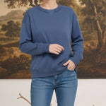 A woman wearing a graced indigo crewneck pullover with ribbed trim and panel detailing, styled with blue jeans.