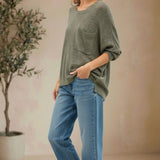 Model wearing a graced forest green dolman long sleeve knit sweater with a chest pocket and relaxed fit with blue jeans