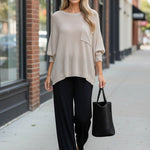 Model wearing a graced pebble dolman long sleeve knit sweater with a chest pocket and relaxed fit on a city street.