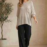 Model wearing a graced pebble dolman long sleeve knit sweater with a chest pocket and black trousers in a studio.