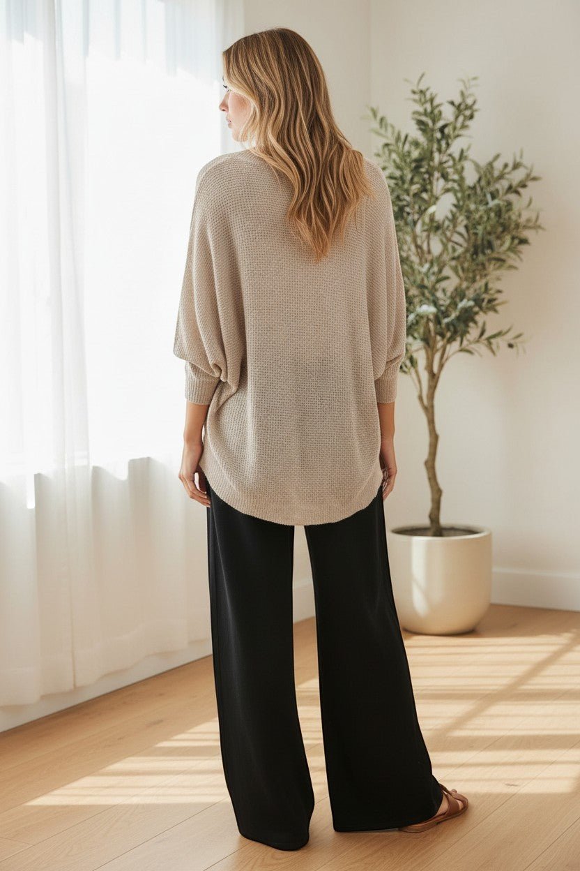 graced dolman long sleeve knit sweater in pebble beige worn by a woman with black wide-leg trousers