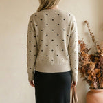 graced beige crewneck sweater with black polka dots worn by a woman with blonde hair from the back view