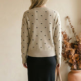 graced beige crewneck sweater with black polka dots worn by a woman with blonde hair from the back view
