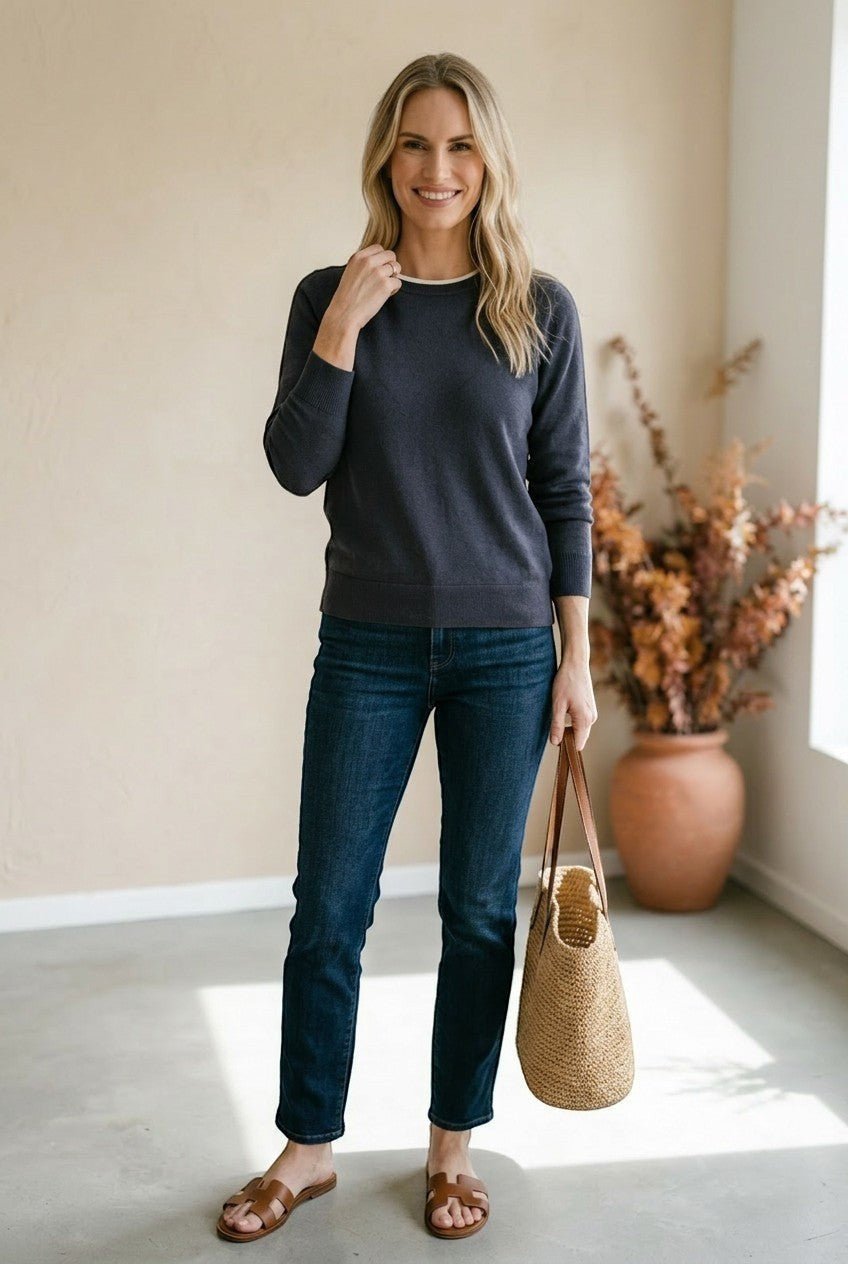 A woman wearing a graced charcoal grey double layered sweater with a white neckline detail, paired with dark blue jeans.