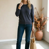 A woman wearing a graced charcoal grey double layered sweater with a white neckline detail, paired with dark blue jeans.
