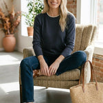 graced double layered sweater in charcoal with white neckline detail worn by a smiling woman in a cozy room