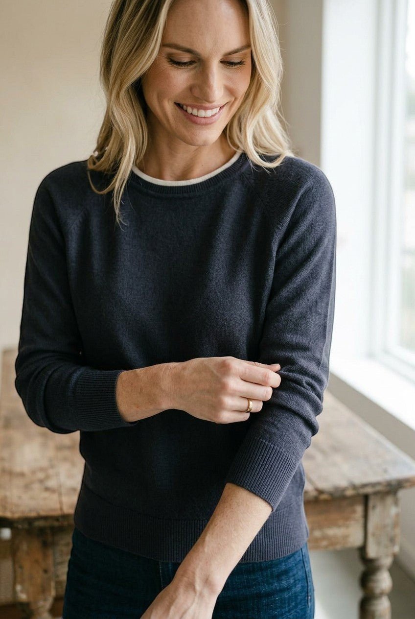graced double layered charcoal sweater with a white neckline detail worn by a smiling woman in a relaxed fit