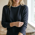 graced double layered charcoal sweater with a white neckline detail worn by a smiling woman in a relaxed fit