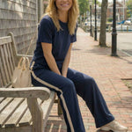 Woman sitting on a bench wearing a navy outfit with white stripes in an urban setting.