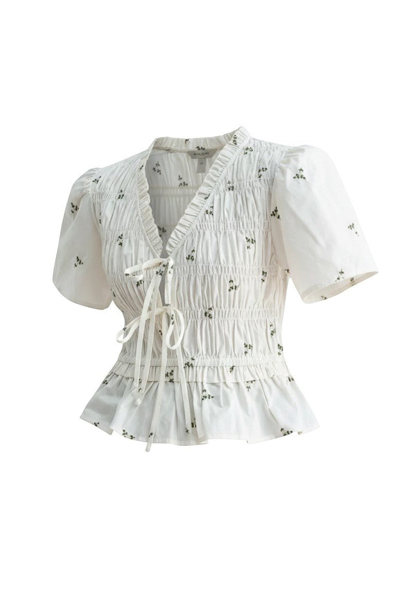 White embroidered peplum blouse from Camellia featuring pleated details and intricate embroidery, styled as a fashionable women's top.