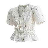 White embroidered peplum blouse from Camellia featuring pleated details and intricate embroidery, styled as a fashionable women's top.