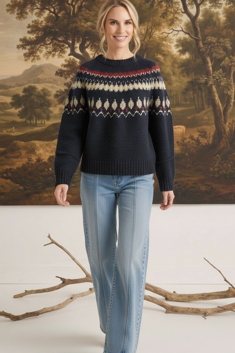 A woman wearing a graced navy blue Fair Isle crew neck sweater with a geometric pattern, paired with light wash jeans.