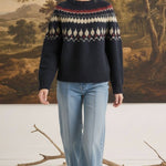 A woman wearing a graced navy blue Fair Isle crew neck sweater with a geometric pattern, paired with light wash jeans.