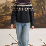 A woman wearing a graced navy blue Fair Isle crew neck sweater with a geometric pattern, paired with light wash jeans.