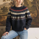 A woman wearing a navy graced Fair Isle crew neck sweater with geometric cream and red patterns, paired with jeans.