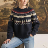 A woman wearing a navy graced Fair Isle crew neck sweater with geometric cream and red patterns, paired with jeans.