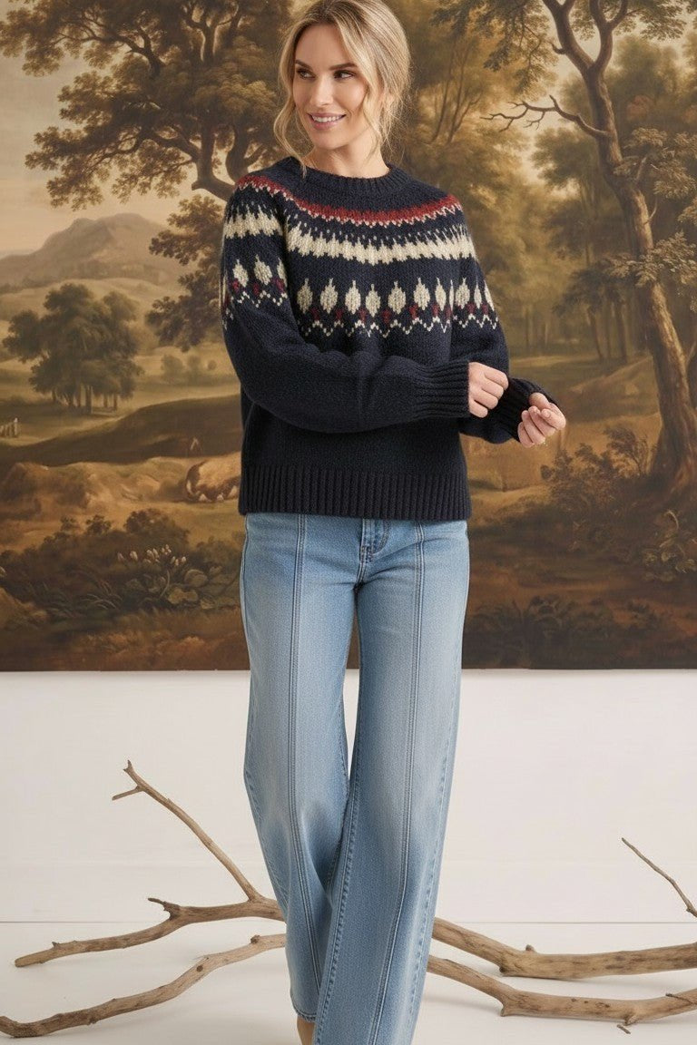 Woman wearing a navy graced Fair Isle crew neck sweater with geometric patterns, paired with light wash wide-leg jeans.