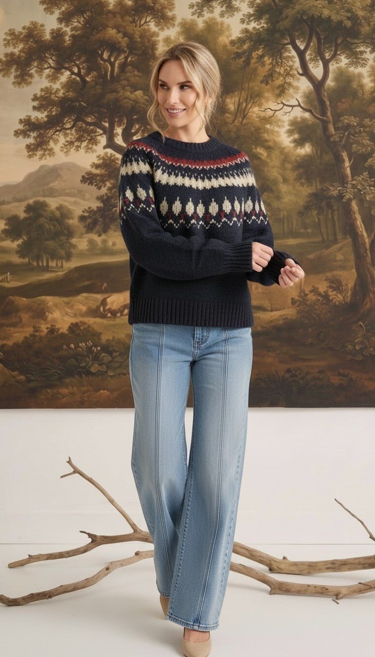 Woman wearing a navy graced Fair Isle crew neck sweater with geometric patterns, paired with light wash wide-leg jeans.
