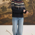 Woman wearing a navy graced Fair Isle crew neck sweater with geometric patterns, paired with light wash wide-leg jeans.