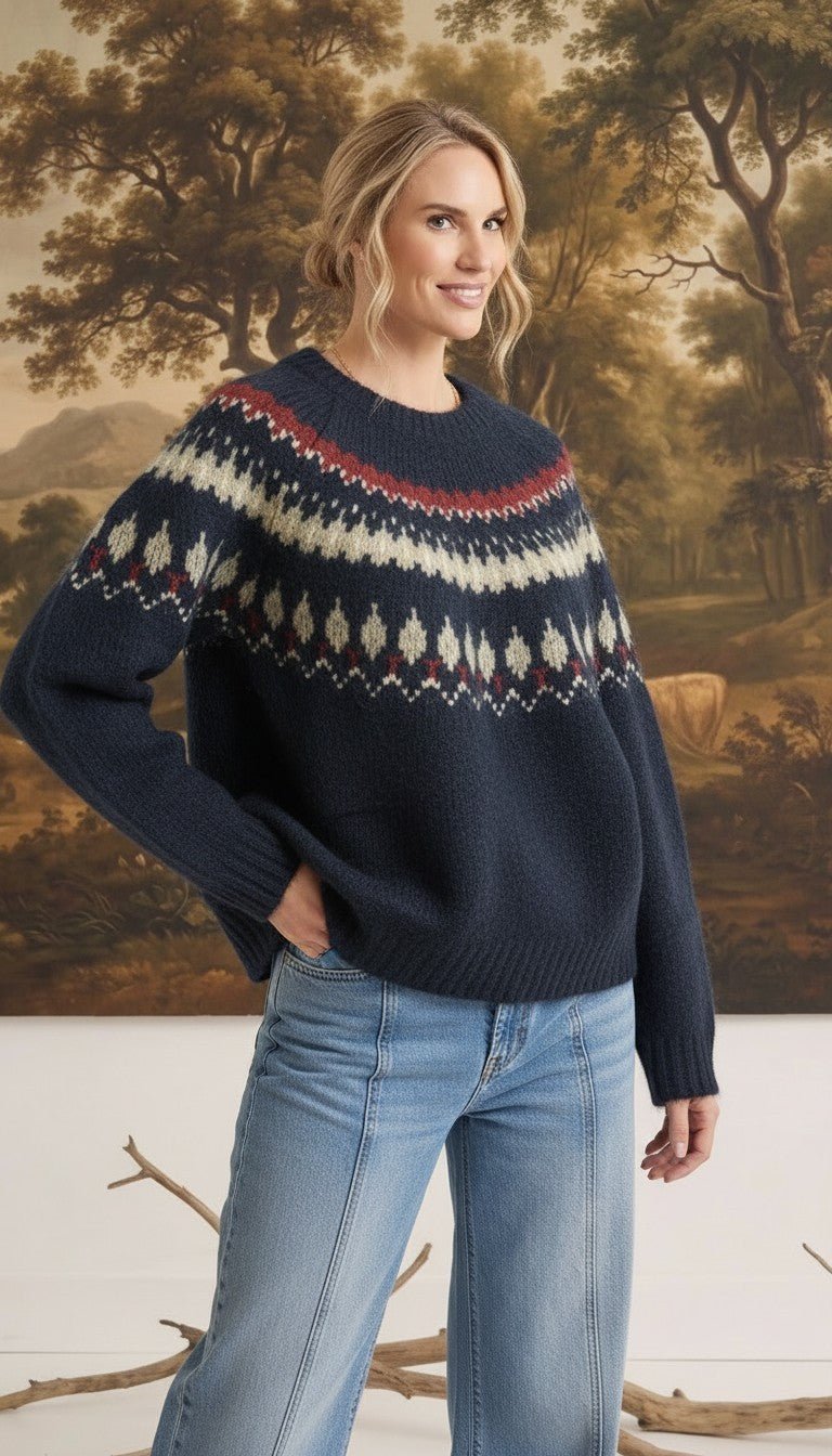 Woman wearing a navy graced Fair Isle crew neck sweater with red and cream geometric patterns, paired with blue jeans.