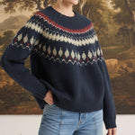Woman wearing a navy graced Fair Isle crew neck sweater with red and cream geometric patterns, paired with blue jeans.