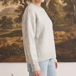 A woman wearing a graced light grey pullover sweater with delicate white floral embroidery on the sleeve and front.