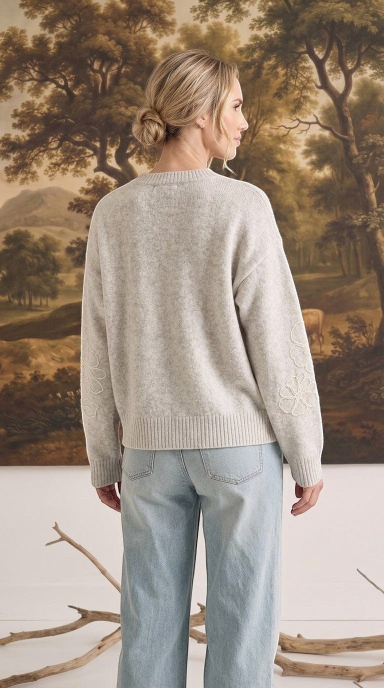 Woman wearing a graced beige pullover sweater with delicate floral embroidery on the sleeves, back view.
