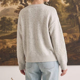 Woman wearing a graced beige pullover sweater with delicate floral embroidery on the sleeves, back view.