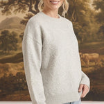 A woman wearing a graced light grey pullover sweater with delicate white floral embroidery and a crew neckline.