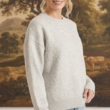 A woman wearing a graced light grey pullover sweater with delicate white floral embroidery and a crew neckline.