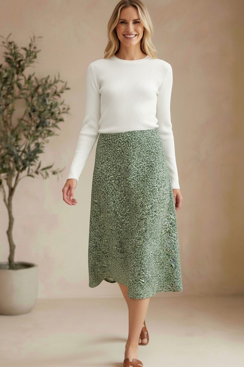 Model wearing a graced green floral print midi skirt with a white ribbed top and brown sandals in a studio setting.