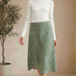 Model wearing a graced green floral print midi skirt with a white ribbed top and brown sandals in a studio setting.