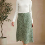 Model wearing a graced green floral print midi skirt with a white ribbed top and brown sandals in a studio setting.