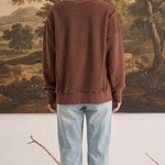 Back view of a woman wearing the graced Ashley oversized chocolate brown fleece top with light wash jeans