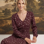 graced Audrey midi dress in burgundy with white floral print, v-neckline, and long sleeves on a seated model