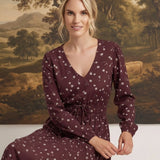 graced Audrey midi dress in burgundy with white floral print, v-neckline, and long sleeves on a seated model
