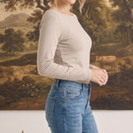 Woman wearing a graced beige long sleeve boat neck knit top with blue jeans in a studio setting