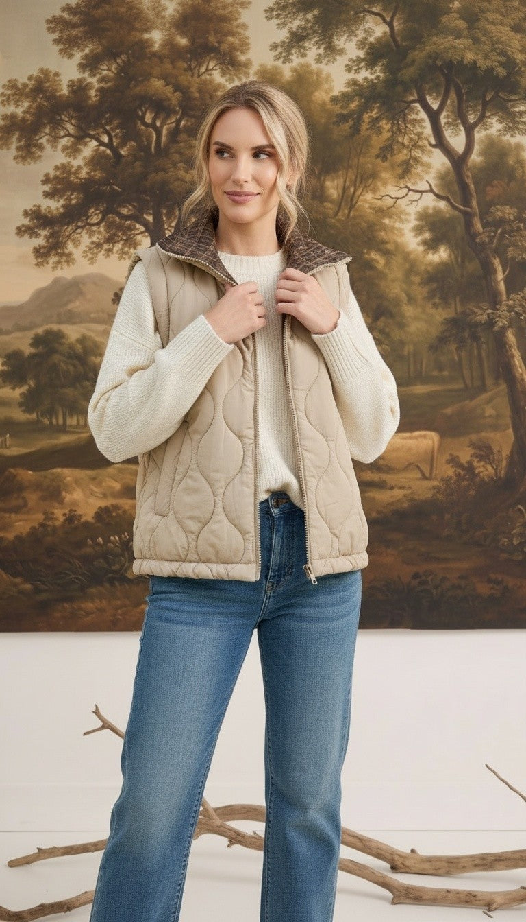 A model wearing a graced beige quilted vest with a plaid collar over a white sweater and blue jeans.