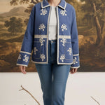 Model wearing a graced blue cotton jacket with white floral embroidery and lace trim over a white top and blue jeans.