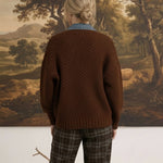 Back view of a woman wearing a graced brown cable knit jacket with denim collar detail and plaid trousers.