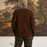 Back view of a woman wearing a graced brown cable knit jacket with denim collar detail and plaid trousers.