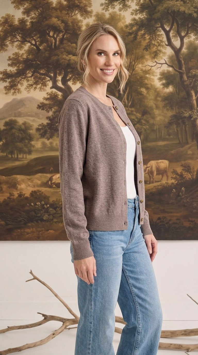 Woman wearing a graced brown crew neck button down cardigan over a white top and blue jeans in a studio setting