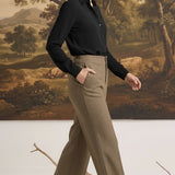 A woman wearing graced houndstooth knit straight pants in brown paired with a black blouse in a studio setting.
