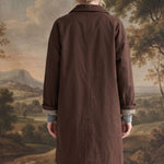 Back view of a woman wearing a graced brown midi trench coat with cuffed sleeves revealing a gingham lining