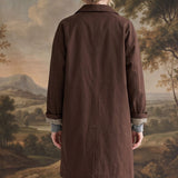 Back view of a woman wearing a graced brown midi trench coat with cuffed sleeves revealing a gingham lining